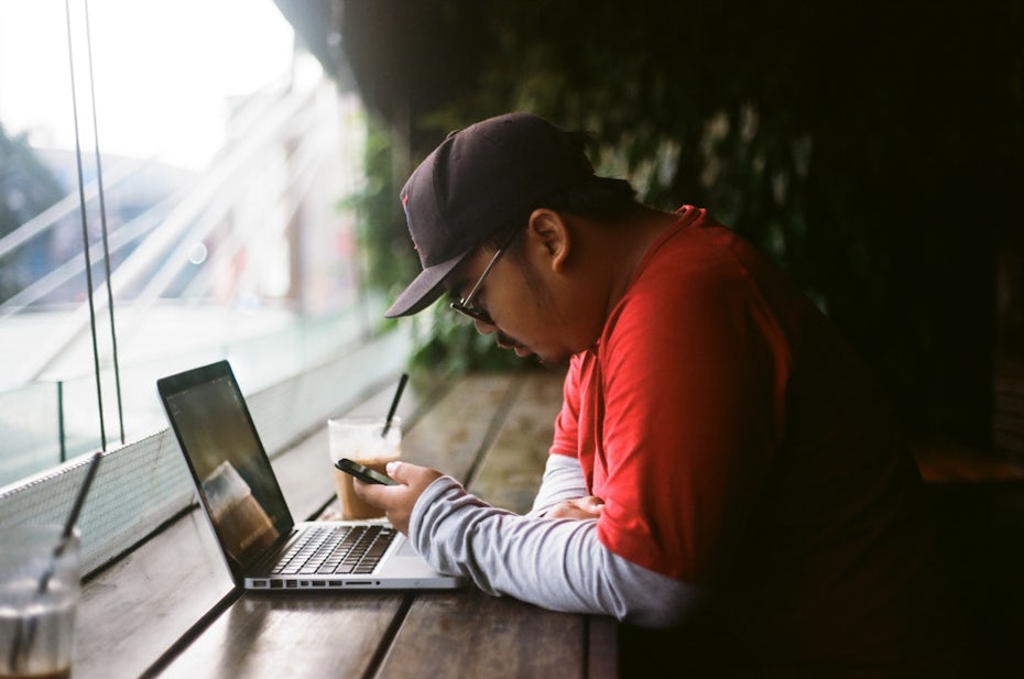 Man sitting alone with his phone, laptop and an iced coffee.