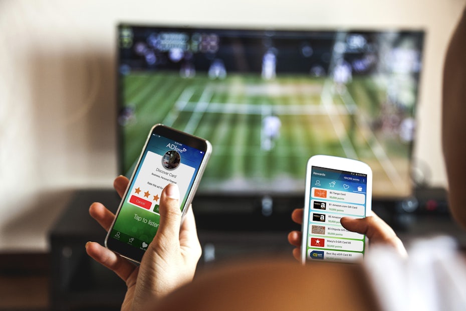 Couple sitting on a couch, smartphones in hand, using an app while watching sports