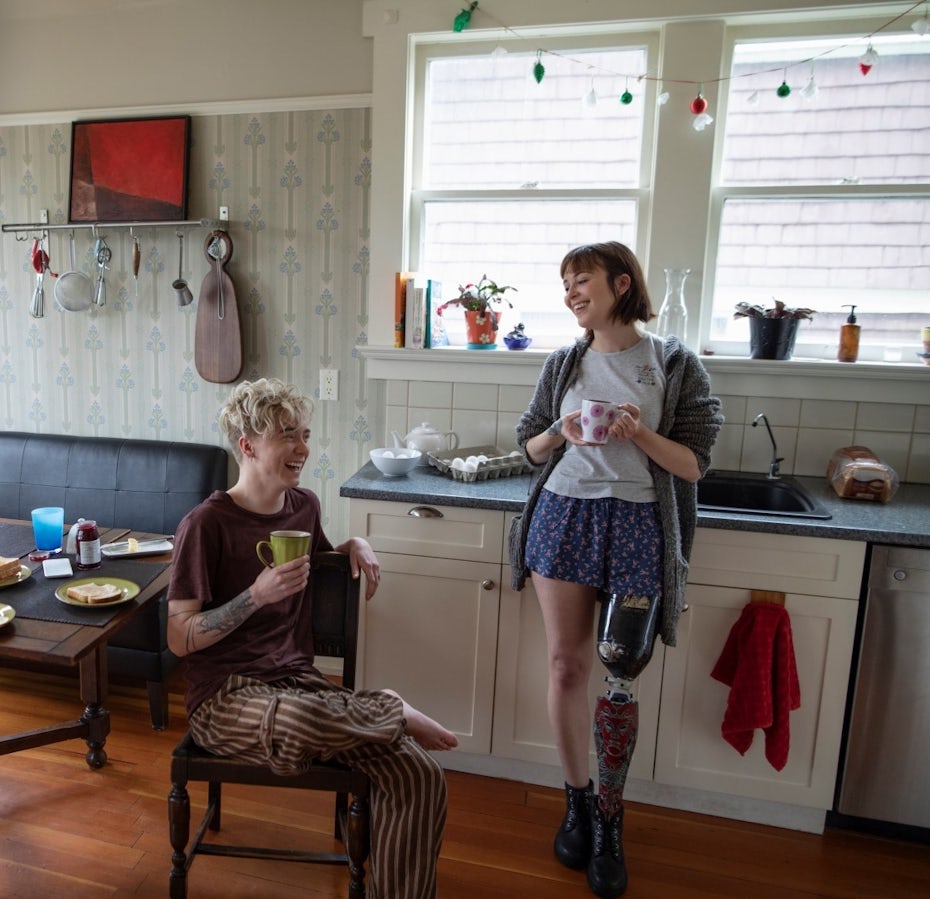 A woman with a prosthetic leg drinking coffee, talking with boyfriend in kitchen