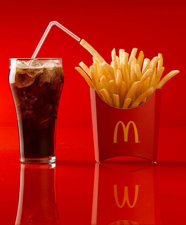 glass of coke next to a McDonald’s french fries against a red background