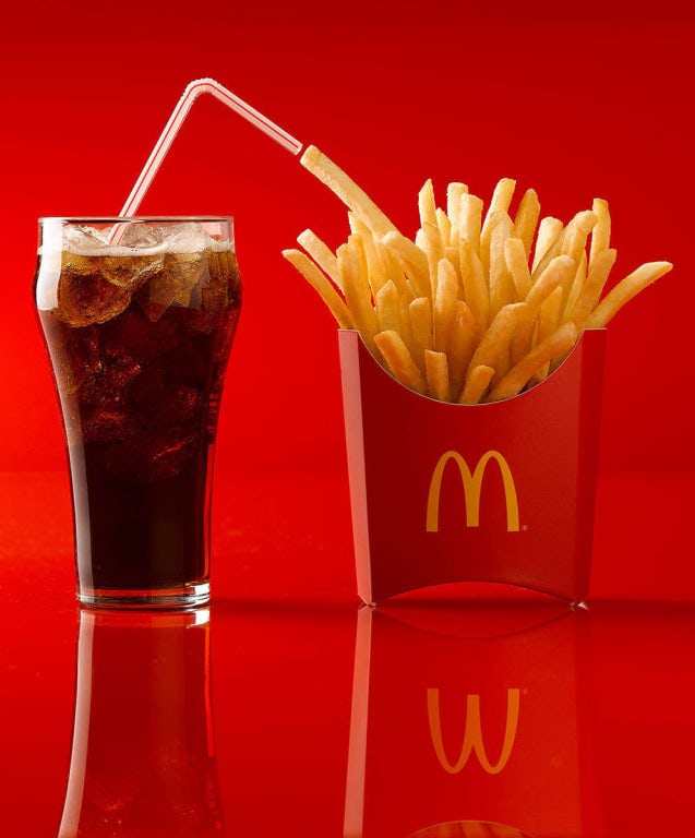 glass of coke next to a McDonald’s french fries against a red background