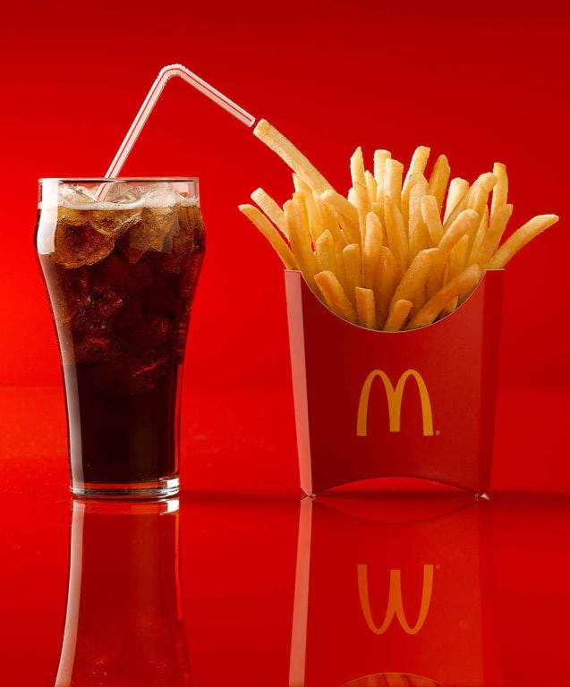 glass of coke next to a McDonald’s french fries against a red background