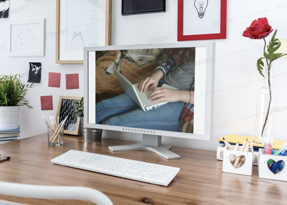 Desktop monitor on a desk with pencils, markers and a rose beside it, picture frames on the wall