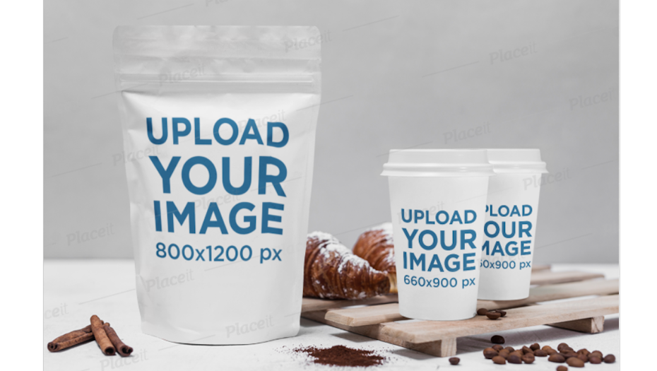 pouch packaging beside two paper coffee cups, resting beside coffee beans, cinnamon and croissants