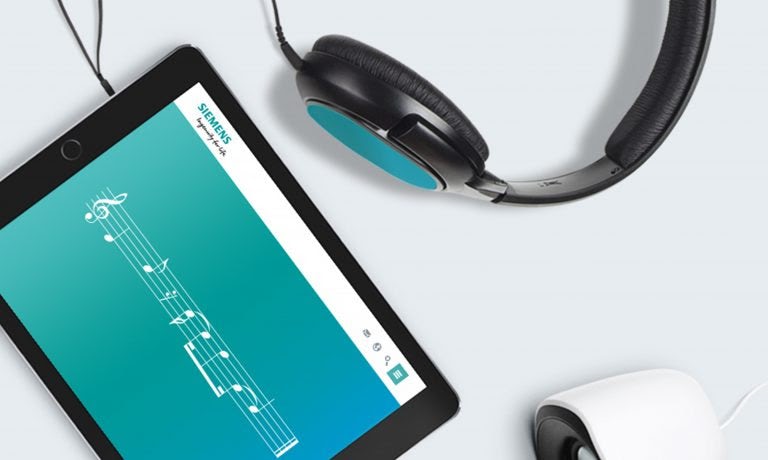 a tablet is open with the musical notes to Siemens’ audio branding on display, and a black and blue headphones on the side