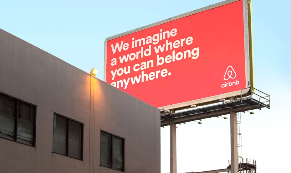 an airbnb billboard in coral pink and a text that says: we imagine a world where you can belong anywhere.