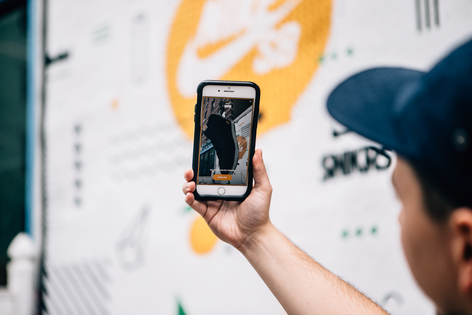 A man wearing a black cap points his iPhone camera at an SNKRS poster to buy a pair of black Nike shoes.
