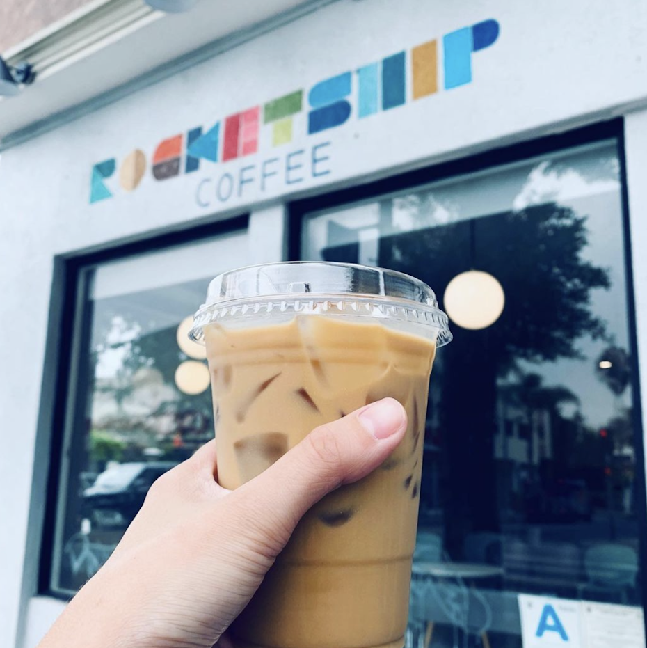 a person holding a cup of iced coffee infront of rocketship coffee
