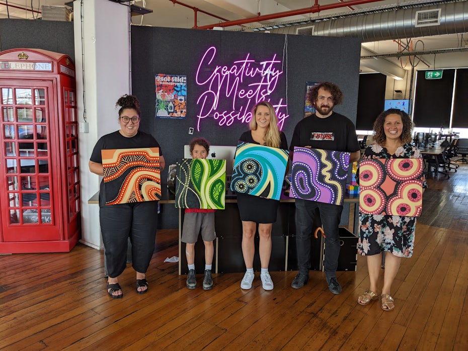 five people each holding up a piece of artwork in the 99designs fofice