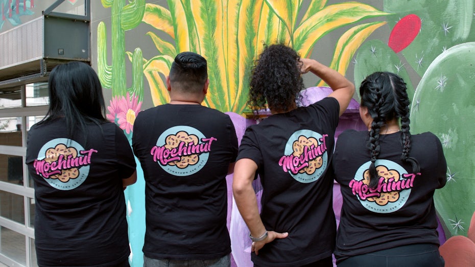 Photo of Mochinut staff wearing a Mochinut branded shirts in front of a San Jose mural