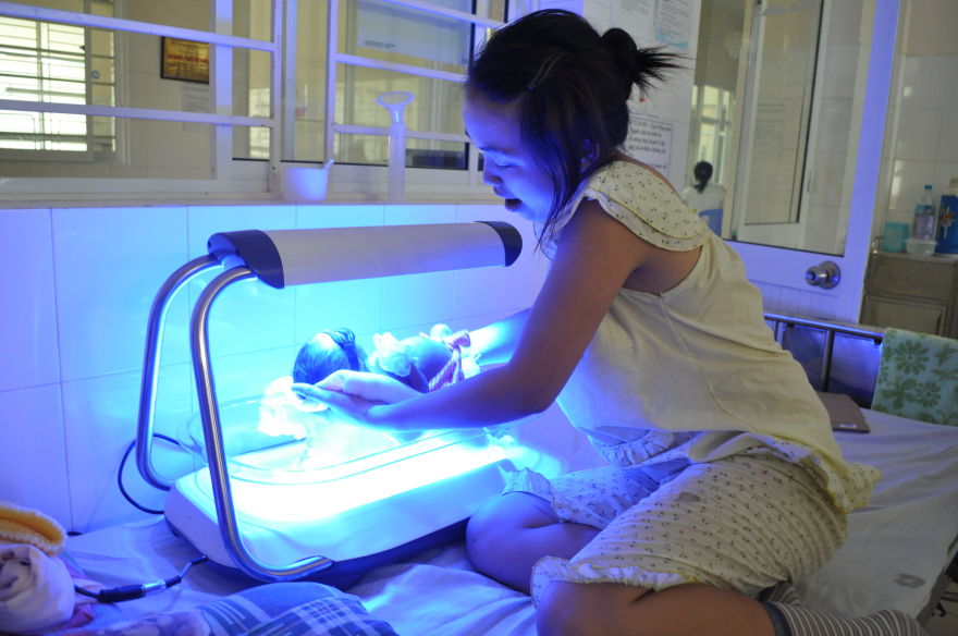 Photo of a mother placing her baby in the Firefly lamp bed to combat jaundice