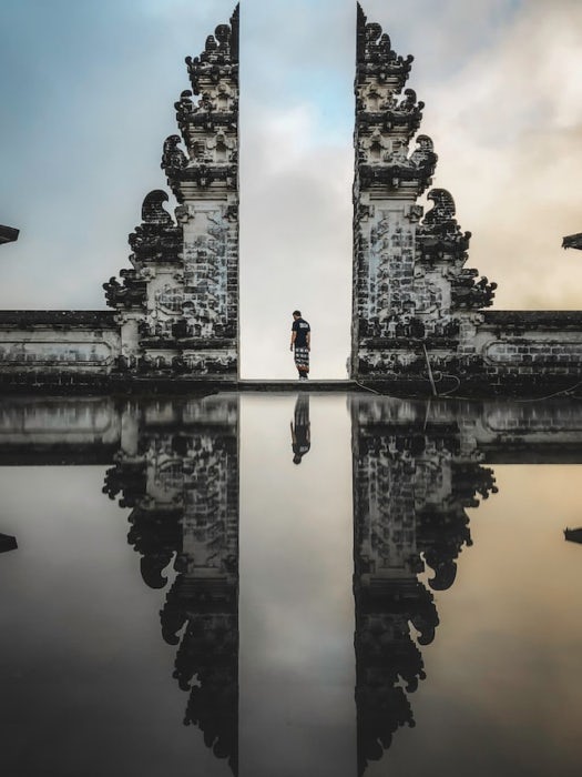 photo of a person standing between two stone structures of a temple in Bali