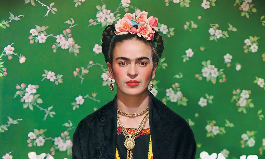 Frida Kahlo color photograph in front of a floral wallpaper